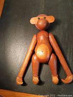 Front view of articulated teak monkey on dark surface