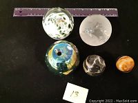 Five paperweights with a ruler for scale, showing varied colors and designs