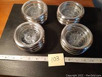 Set of 12 round silver plated coasters with glass centers arranged in four stacks on a black surface with ruler for scale.