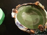 Top angled view of 5 inch pottery bowl showing green glazed interior and three small sculptural figures around undulating rim, each with detailed faces and hairstyles.