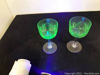 Photo showing two uranium cut crystal wine glasses glowing green under UV light, demonstrating fluorescent property.
