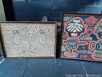 Photo of both framed Cuna Mola textile art pieces side by side on floor showing overall appearance and frame condition.