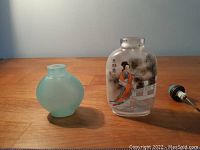 Two old snuff bottles on wooden surface, one green translucent and one opaque with painted interior