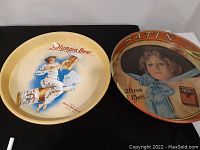 Two round vintage beer advertising trays displayed side by side, one for Olympia Beer and other for Satin Cigarettes.