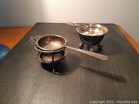 View of both metal tea strainers and their stands placed on a flat surface.