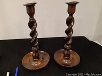 Pair of antique wooden barley twist candle holders standing on black cloth background, showing full view of both items.