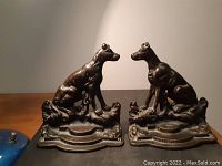 Pair of antique metal bookends depicting seated hunting dogs on a decorative base, shown side by side.