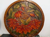 Full view of the circular wooden pyrography panel with red-orange flowers and green leaves on textured wood background.