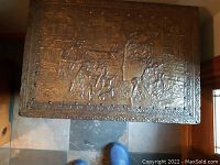 Top view of antique brass firewood box showing detailed embossed scenes of figures and surroundings.