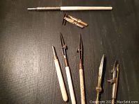 Photo of the entire set of antique drafting tools laid on a dark surface. Includes wooden and metal components such as compasses, pens, and nibs.