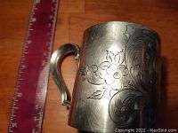 Front and side view showing floral and scroll engravings and handle with a ruler in the background for size reference.