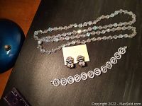 Full set displayed on a black surface showing necklace, earrings on card, and bracelet side by side.