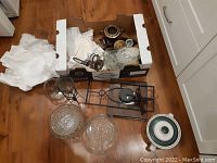 View of box with various bowls, metal items, glassware, and a ceramic pot with lid on wooden floor
