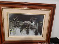 Full view of the framed print of a loon depicting a water scene with reeds and reflections.