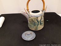 Side view of the teapot with lid removed. Shows blue and beige glaze with artistic design and bamboo handle.