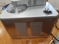 Side view of silver Cuisinart ice cream maker showing vents, control knob and Cuisinart logo