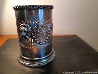 Front and side view of silver plated cylindrical holder showing pierced design and lion mask with ring