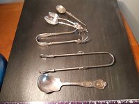 Full view of the six items laid out on a flat black surface, showing the spoon set and tongs.