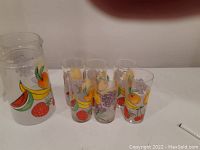 Full shot of the glass jug and six glasses with colorful fruit designs