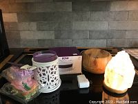 Photo showing wax melts, ceramic wax melt warmer with purple wax inside, wooden oil diffuser, selenite salt lamp.