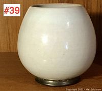 Front view of the white globe-shaped pottery vase with a metal base on wood background.