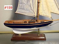 Side view of vintage wooden model sailboat showing blue hull and white sails on wooden base with brass supports.