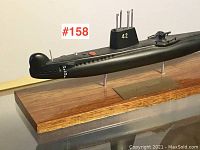 Side view of black vintage submarine model on wooden base, showing profile and metal plaque.