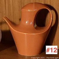 Orange mid century modern Japanese pottery coffee pot with large loop handle and angular spout on shelf.
