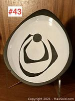 Front view of triangular pottery dish showing abstract black design on white glazed interior with dark unglazed rim.