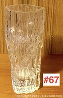 Clear textured glass vase with vertical ridges and organic form shown from front on wooden surface.