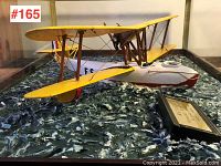 Side view of the yellow biplane flying boat model and textured sea surface diorama base in glass case