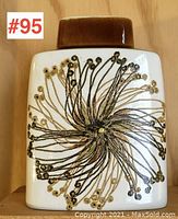 Front view of square vase with brown top and gold-black floral/starburst pattern on white body.