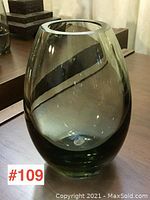 Full view of the vase showing its rounded oval form, tinted dark green glass, and polished metal rim.
