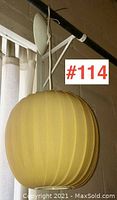 Side view of the yellow plastic ball pendant ceiling lamp hanging from a white ceiling mount and cord.