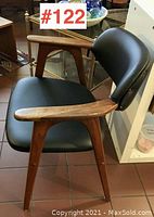 Three-quarter front view showing teak frame, armrests, black vinyl seat and back.