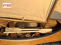 Close-up of the interior of the model sailboat showing wood slatted deck, two white oars laid across, coiled rope, and rigging detail.