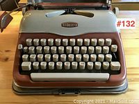 Front view of typewriter on metal base tray showing keybed, brand emblem and overall condition