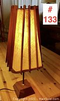 Front three-quarter view of teak table lamp illuminated on wood surface