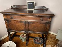 Full front view of antique sideboard cabinet showing drawer, two door compartments, carved legs, and claw feet on wood floor.
