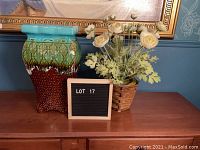 Front and side view of ceramic pedestal with brown woven basket planter holding white faux flowers on wooden surface