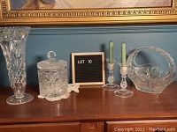 Five vintage crystal pieces including tall vase, ice bucket with lid, candy dish with handle, and two taper candle holders arranged on wood surface.