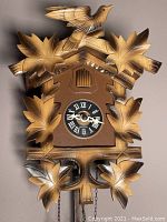 Front view of brown plastic cuckoo clock with carved maple leaves and bird on top. Clock shows time and Roman numerals.