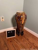 Full view of multi-colored floor vase on wooden stand beside a lot number sign.