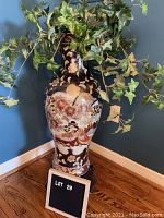Full view of the Asian motif floor vase on a wooden stand with faux ivy plant inside.