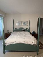 Front view of green painted queen size four poster bed with bedding and two nightstands visible on each side
