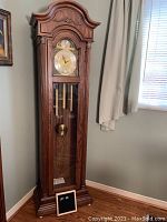 Full front view of the tall wooden grandfather clock in room corner