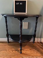 Front view of dark wooden half-moon hall table with bevelled edges and turned legs, showing shelf below.