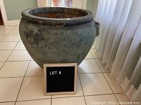 Full view of large green ceramic planter showing rounded body and wide opening on white tiled floor