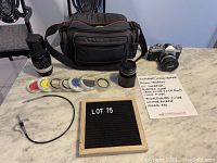 Overview of Nikkormat camera with two lenses, multiple filters in plastic sleeves, a cable release, and camera bag on marble surface.