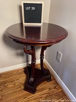 Front view of the round mahogany occasional table showing the smooth polished surface and pelican-head carved legs on a hardwood floor near a corner wall.